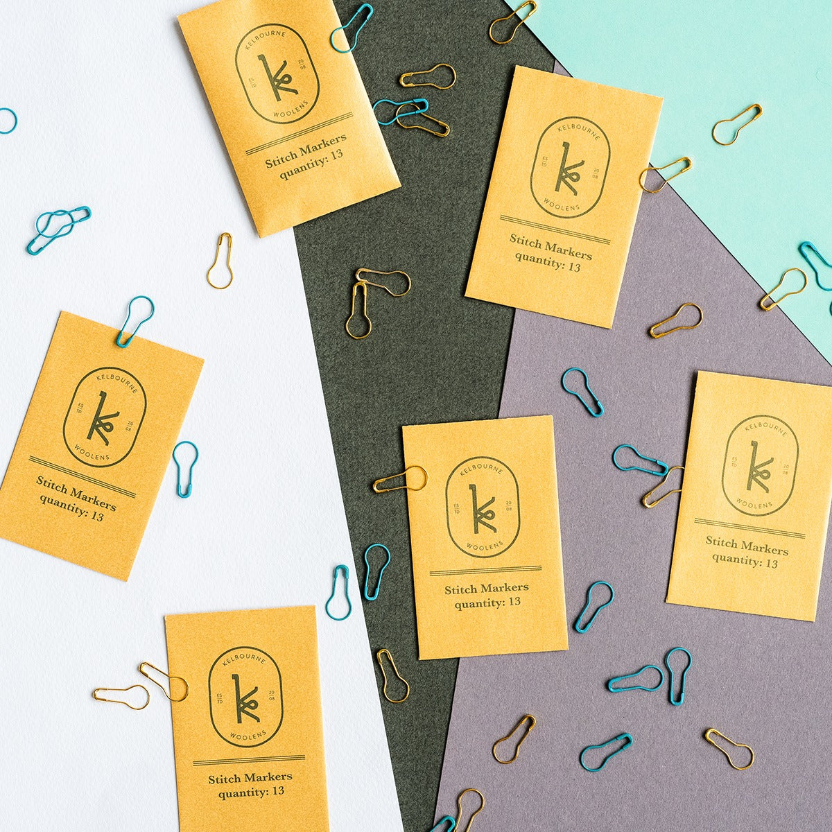 Teal blue and gold stitch markers scattered on a colorblocked background