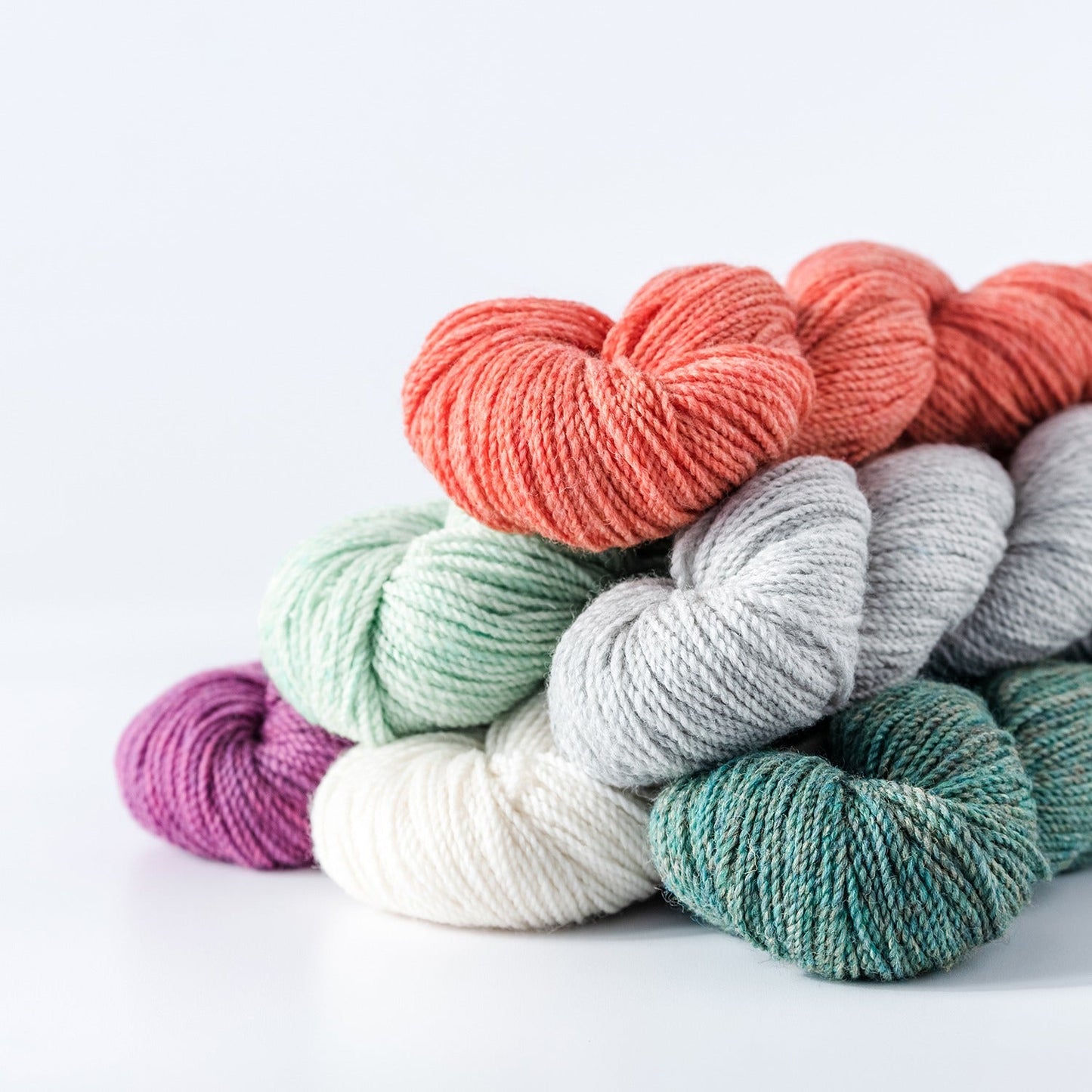 skeins of kelbourne wools fingering weight wool yarn in a pile on a white background