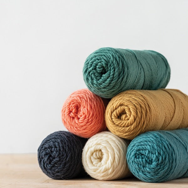 Stack of Kelbounre Woolens Germantown N. American wool yarn in black, white, gold, turquoise, and coral on a wood ground with light gray background
