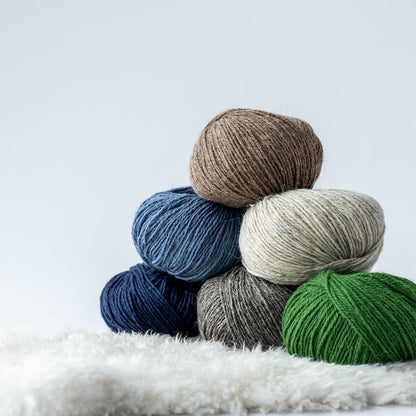 Beauty shot of wool yarn Navia Tradition in green, natural greys, and blue on a shearling ground with light grey background